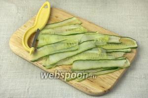 Огурцы нарезать очень тонкими продольными пластинами. Сделать это можно при помощи ножа для чистки овощей или специальной тёрки.