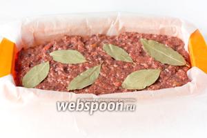 На дно узкой прямоугольной формы для запекания паштета выкладываем лист пергамента для выпечки так, чтобы края свисали по обе стороны. Далее выкладываем в форму подготовленную паштетную массу, разравниваем поверхность, на которую выкладываем лавровые листы.