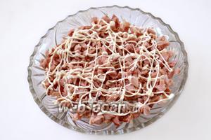 Кусок копчёной курицы разделываем, удалив кожицу и кости. Куриное мясо нарезаем мелкими кубиками. Укладываем половину курицы в салатник, нанеся майонезную сеточку.