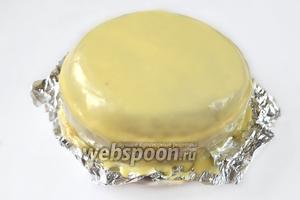 Под нижний корж подкладываем кусочки фольги, чтобы сохранить чистой тарелку. Заливаем торт белым ганашем, разглаживаем с помощью фена при средней температуре и низкой скорости.