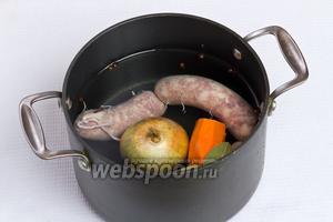 Теперь приступаем к приготовлению самого супа. Для этого кладём в кастрюлю колбасу, нечищенный лук, очищенную морковь, лавровые листы, гвоздику и перец горошком. Далее заливаем водой и варим 30 минут.
