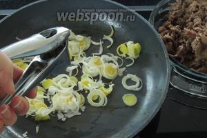 Вынимаем мясо, подсаливаем по вкусу. В той же сковороде ещё 1/2 ст. л. масла подогреем. Кладём нарезанный кольцами лук-порей и выжимаем зубок чеснока. Обжарим около 1 минуты.