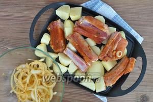 Картофель резать не мелко и не крупно, а на такие кусочки, которые должны успеть пропечься за 40 минут. Посолить. Смазать растительным маслом сковородку и выложить картофель. Сверху рёбра, а лук пока не выкладывать. Поставить в духовку при 190 ºC на 20 минут. Через 20 минут добавить лук перемешать и перевернуть рёбра. Запекать ещё 20 минут.