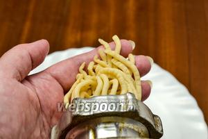 По частям пропускаем тесто через механическую мясорубку. Выходящие из решётки червячки теста придерживаем одной рукой и, когда они достигнут размера 5 сантиметров, отрезаем у решётки ножом.