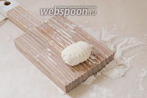 Специальную доску для пасты посыпаем мукой и большим пальцем скатываем творожный шарик вдоль борозд на доске.