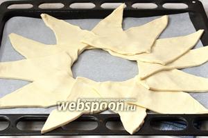 В форму для выпекания выложить кулинарную бумагу. На бумагу внахлёст выкладывать треугольники (слегка вытянув концы треугольников) таким образом, чтобы образовался круг диаметром 8-10 сантиметров.