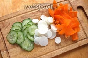 Нарежьте огурцы и дайкон очень тонкими кружочками, нарежьте морковку с помощью «экономки» тонкой длинной стружкой.