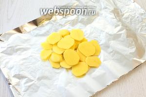 Фольгу сложить вдвое, серединку смазать маслом. Очищенный картофель нарезать тонкими ломтиками толщиной от 0.3 до 0.5 см и уложить на фольгу. Посолить слегка.