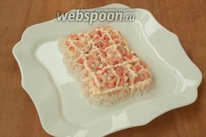 Сваренные креветки почистить, нарезать кубиком крабовые палочки. Выложить их произвольно сверху риса и снова нанести майонез.