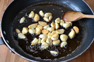 В сковороду, где обжаривалась курица, выложить зубчики чеснока. Огонь убавить до слабого. Обжаривать чеснок минут 5-7, постоянно помешивая! Это важно, иначе чеснок подгорит, а он должен стать равномерного золотистого цвета.