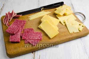 Готовить это блюдо, желательно, в перчатках. Сделать выкройку-прямоугольник из бумаги в клетку размером 6х3 см. Сложить в стопку сыры и колбасу. Приложить выкройку и острым ножом нарезать прямоугольники нужного размера. Сыр с гладкой поверхностью используем на верх косточки домино. Второй сорт сыра будет служить основой.
