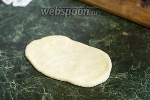Сформованный и подошедший шарик теста для булки распластываем на столе, смазанным маслом, в овал.