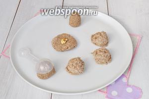 Отмеряя смесь мерной ложкой (объём 1 столовая ложка), выкладывать заготовки на блюдо. Формировать шарик. Прижать его ладонями. Положить в центр орех. Сформировать кейк попс в форме бутона цветка.
