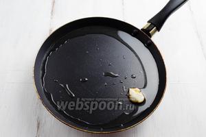 На сковородку влить растительное масло и немного дать ему прогреться. Зубчик чеснока очистить, расплющить ножом. Обжарить чеснок на масле в течение 2-3 минут. Чеснок немного ароматизирует масло.