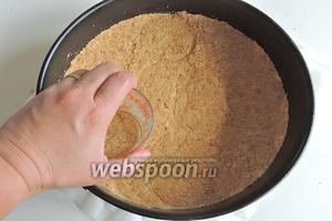 На дно разъёмной формы выкладываем печенье и утрамбовываем. Удобно это делать со стаканом, плотно придавливая его ко дну.
