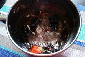 Переложим кусок мяса в подходящую кастрюлю. Вольём сухое красное вино, чернослив, чеснок и чили. Добавим соль, можжевеловые ягоды, душистый перец.