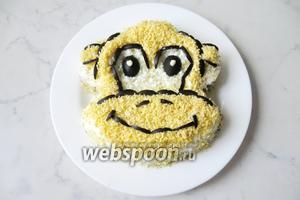 Ушки также выложите с помощью маслин, а верх ушей — тёртым твёрдым сыром. На фото это не видно, потому, что он такой же жёлтый, как желтки. Глазки сделайте из маслин, а зрачки из майонеза. Салат «Обезьяна» готов. Можно добавить бант из листьев салата и маслины. Голову украсить укропом или петрушкой, имитируя волосы.