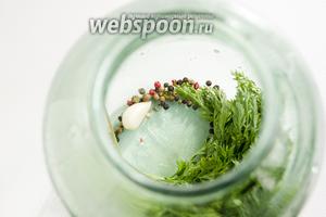 На дно чистой банки поместите чистую ботву моркови, очищенный зубок чеснока, душистый перец и смесь перцев.