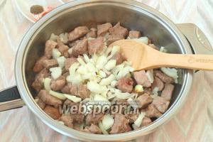 В сковороде разогреть подсолнечное масло, выложить в него кусочки свинины и следом нарезанный четвертькольцами лук. Обжарить, чтобы мясо немного подрумянилось. Приблизительно это займёт 10 минут. Мясо с луком необходимо перемешивать.