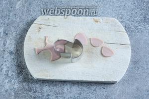 Из тонко нарезанной варёной колбасы вырезаем полукружия. Это можно сделать частью какой-то формочки для печенья (грибочек, сердечко, лепестки цветочков). Если формочек нет, то режем острым ножом вокруг чайной ложки. Это будут уши. Соответственно, их должно быть парное количество штук — в зависимости от количества планируемых голов.