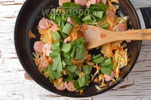 С 2 сосисок снять оболочку. Нарезать сосиски кружочками и отправить их в сковороду. Готовить, помешивая, 1,5-2 минуты. В конце добавить промытую и крупно нарезанную черемшу (0,3 пучка). Готовить 1 минуту.