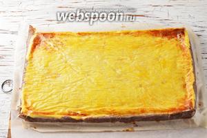 Накрыть форму сверху кухонной доской, выложенной пергаментом. Перевернуть форму на доску. В результате у нас на доске окажется изделие творожной начинкой вверх. Аккуратно снять пергамент с творожной начинки.