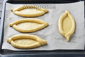 Соединить концы теста с двух краёв, формируя лодочку. Переложить тестяные заготовки на противень с пергаментом. Раздвинуть бортики тестяной заготовки, формируя место для начинки.